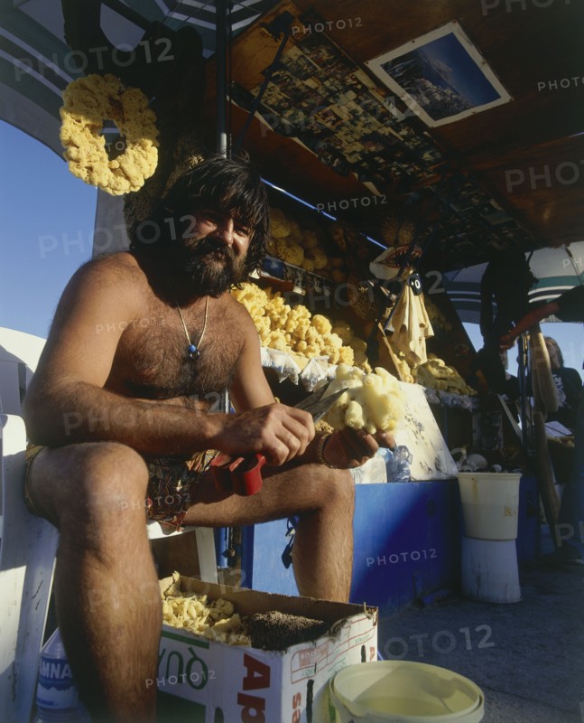 GREECE, Dodecanese Islands, Kos, Kardamina fisherman cleaning sponges at his natural sea products stall