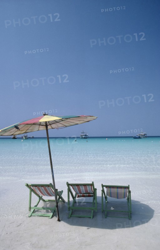 THAILAND, Pattaya , Coral Island, Empty sun loungers and umbrella on beach with boats moored just off shore