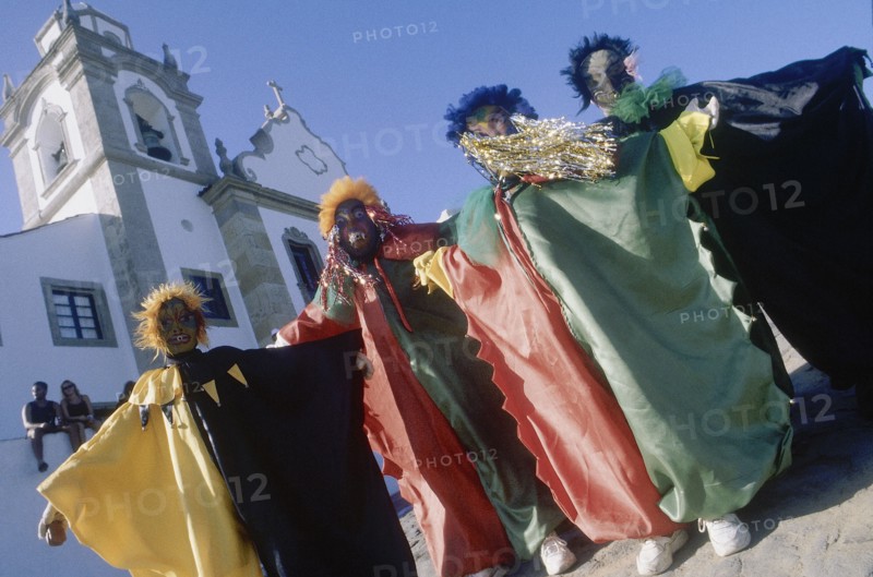 BRAZIL, Pernabuco, Olinda, Four Carnival people in bright costume standing in the street outside a church