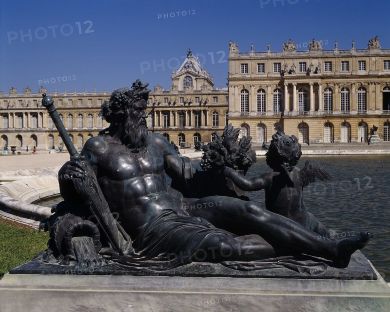 FRANCE, Ile de France, Yvelines, Versailles . Part view of palace behind bronze reclined statue of man with child next to pond