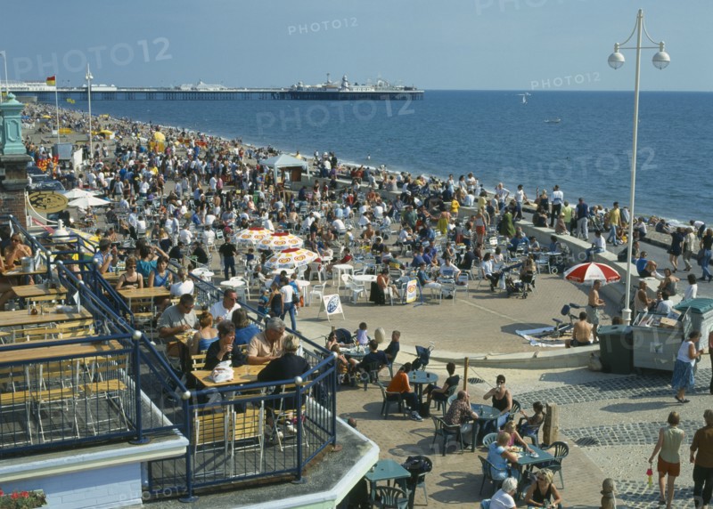 ENGLAND, East Sussex, Brighton, Seafront bars & restaurants with people sitting drinking during the summertime .