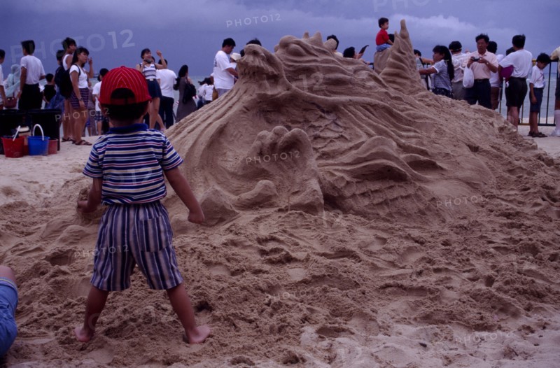 SINGAPORE, Beach, Sand sculpture of a Dragon with a boy standing in front of it holding a handful of sand