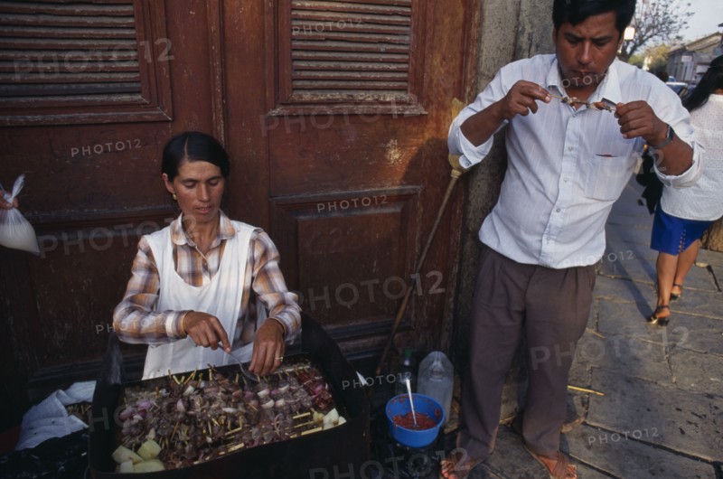 BOLIVIA, Tarija, Women cooking meat skewers on barbecue with man eating nearby