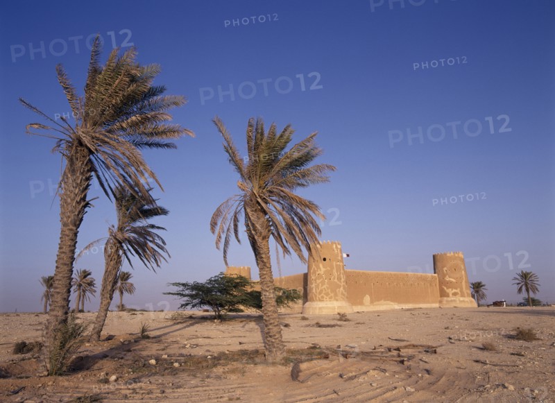 QATAR, Zubara, "Exterior view of a fort with crenellated towers, built in 1938 and used as a police border post, now a museum.  Palm trees in the foreground."