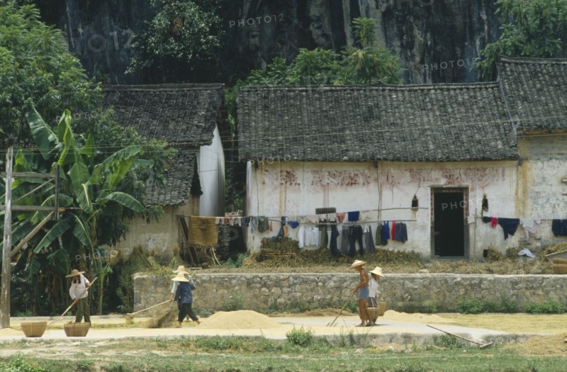 CHINA, Guangxi Province, People drying grain outside a farmhouse.