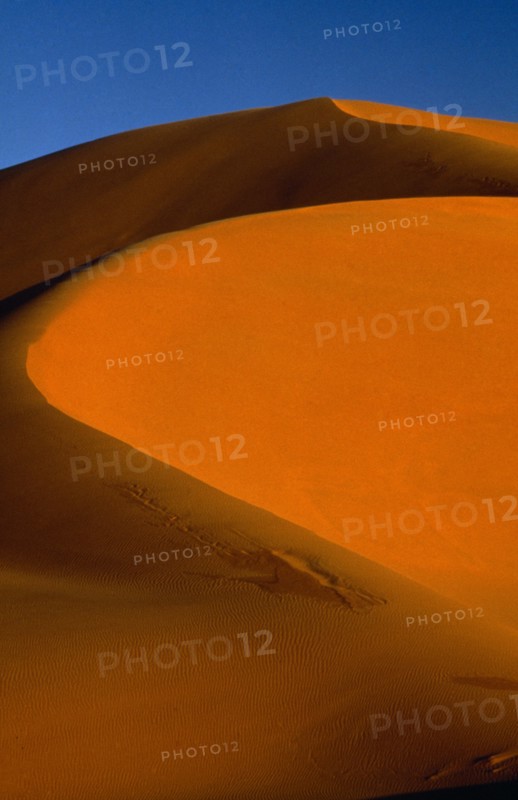 LIBYA, South West , Achan , Orange desert sand dune against a clear blue sky