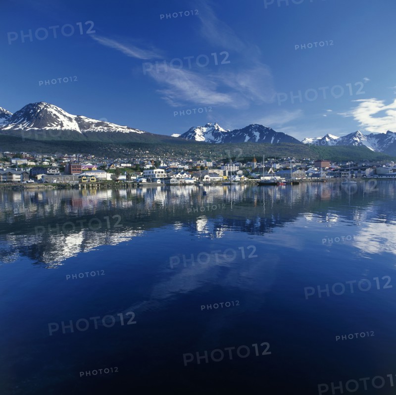 ARGENTINA, Tierra del Fuego, Ushuaia, The town of Bahia Ushuaia reflected in still water with distant snow capped mountains in a typical Patagonian landscape