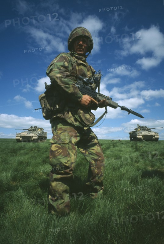MILITARY, Soldier, Training, Soldier in camouflage standing in a field holding a gun with two Warrior tanks behind