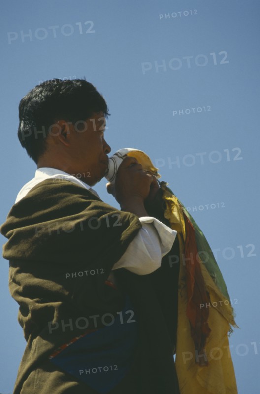 CHINA, Qinghai, Tongren, Tibetan man blowing conch shell at festival