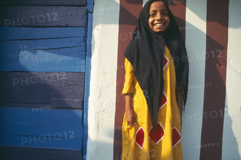 INDIA, Kerala , Kochin, Muslim girl standing in front of building wall painted with red and white stripes.