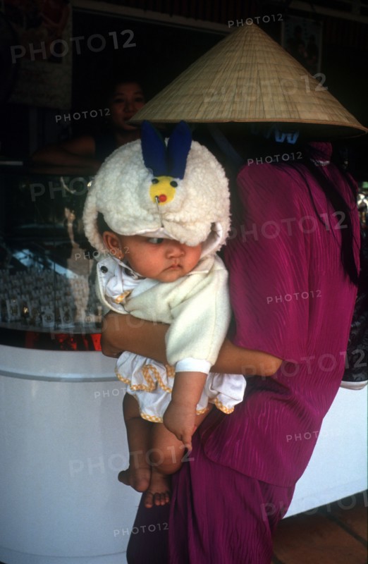 VIETNAM, Tay Ninh, Woman in a straw hat holding a baby as she looks at a shop display in Tay Ninh market.