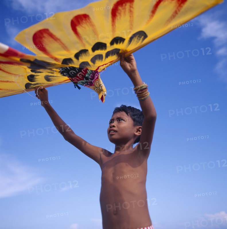 INDONESIA, Lombok, Timur, Young boy holds up a yellow eagle shaped kite
