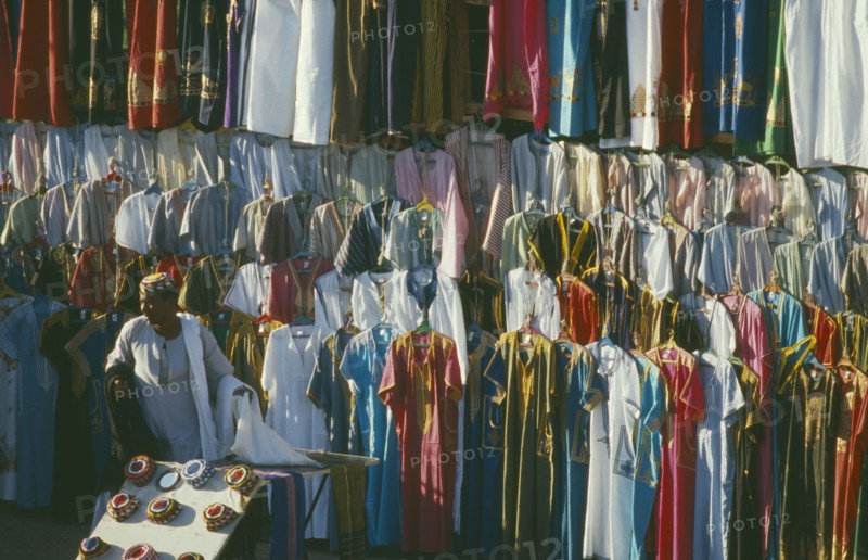EGYPT, Luxor, Clothes stall in market with male vendor standing infront of racks hung with galabeyas.
