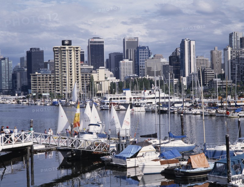 CANADA, British Columbia, Vancouver, City skyline over busy yacht harbour with people walking on the jetty