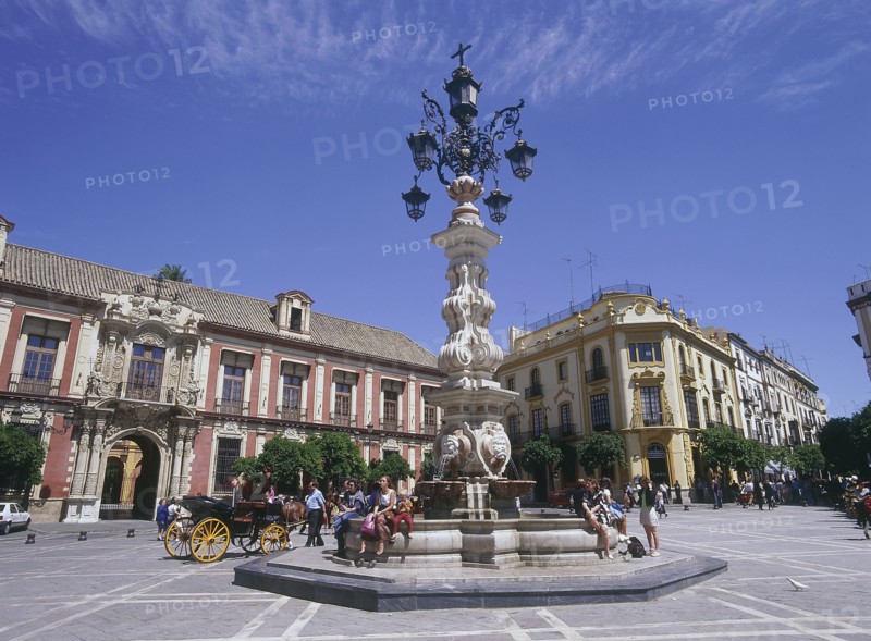 SPAIN, Andalucia, Seville, "Santa Cruz District, Plaza Virgen de los Reyes with Palacio Arzobispal on the left and a horse carriage passing a fountain with people sitting down"