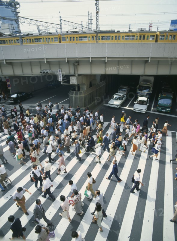 JAPAN, Honshu, Osaka, Umeda District Railway Line over a road with traffic under the bridge and a busy pedestrian crossing in the foreground