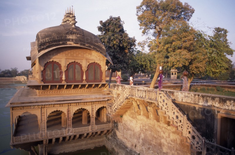 INDIA, Rajasthan , Deeg , "Gopal Bhavan, the Suraj Mahl’s Palace built in the 18th C in Rajput and Mughal style.  Women carrying large jars on their heads across stone wall."