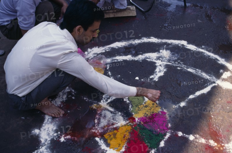 INDIA, Delhi , Man painting wheel-like design on the ground to be used as a base for a bonfire during the Holi Festival.