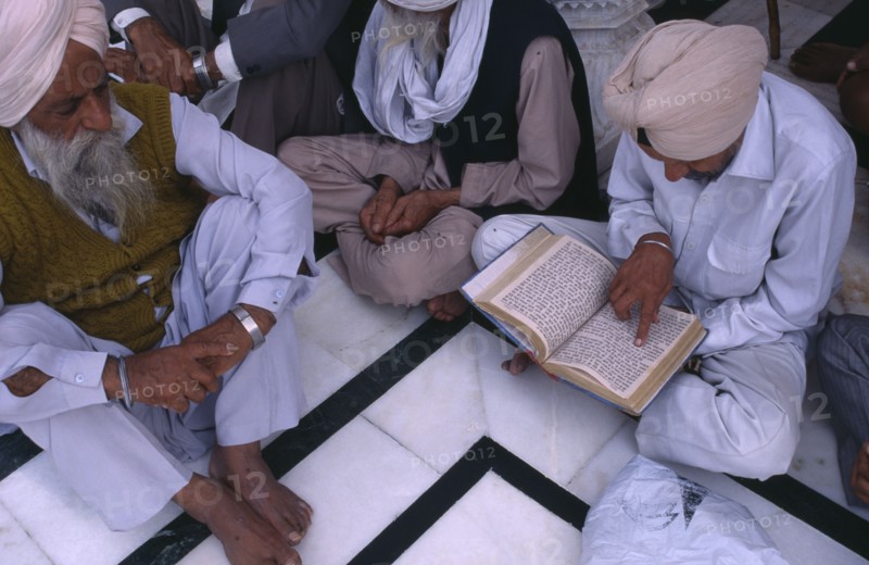 INDIA, Punjab, Amritsar, Group of elderly men reading Sikh holy book at Golden Temple sitting on black and white marble floor..