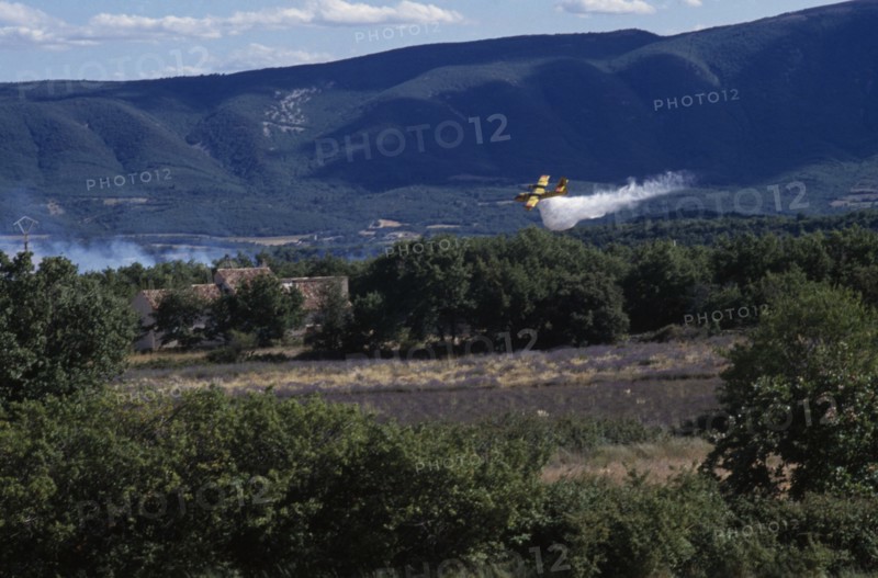 FRANCE, Provence Cote d’Azur, Luberon , Firefighter Plane flying towards smoke from a forest fire rising above green landscape.