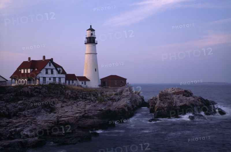USA, Maine, Portland, Portland Head Lighthouse. Waves crashing against rocks seen at dusk in warm light.