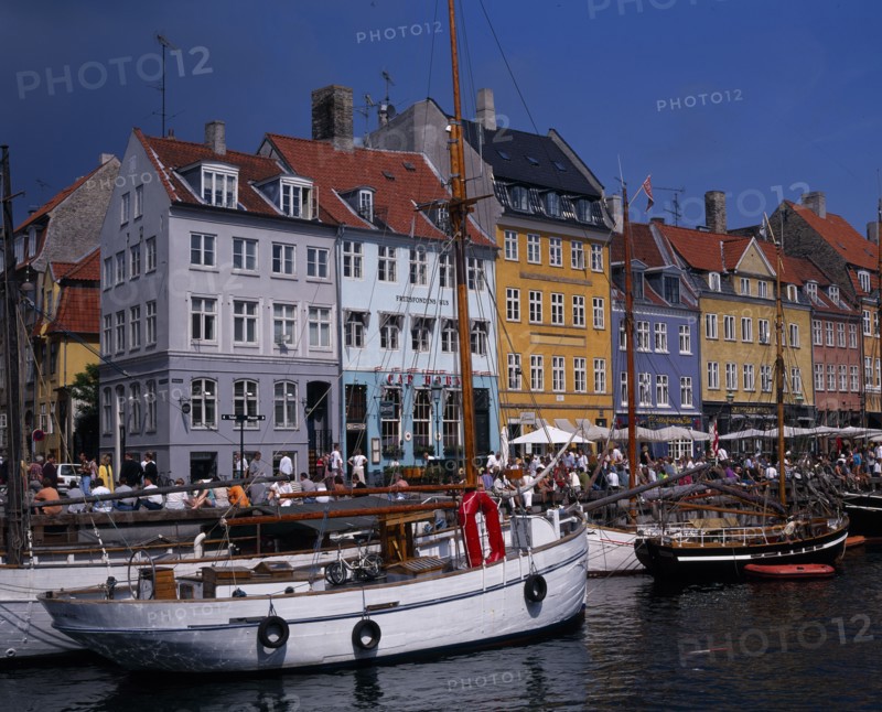 DENMARK, Zealand, Copenhagen, Nyhavn Harbour. Traditional waterfront buildings with crowds of tourists and moored boats on water