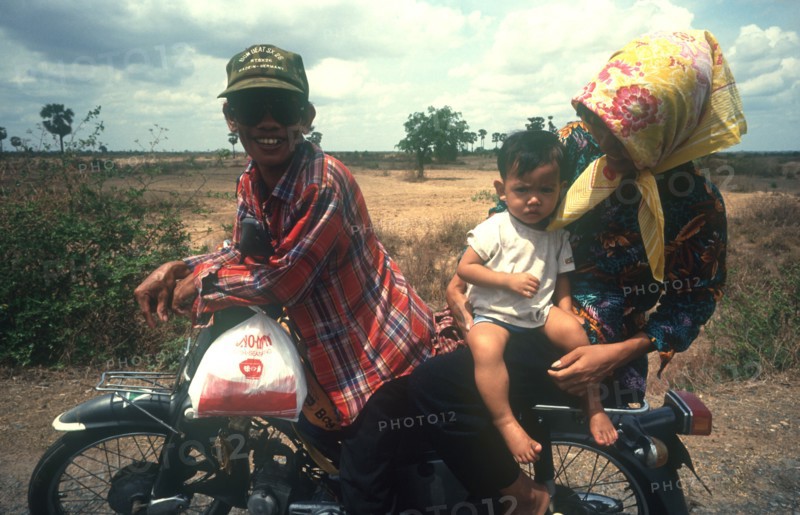 CAMBODIA, Kompong Thom, National Route 6.  Motorbike rider with woman and baby on pillion.
