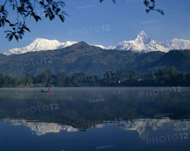 NEPAL, Pokhara, Phewa Lake with mountain peak reflected. Men in boat and branches in the foreground.