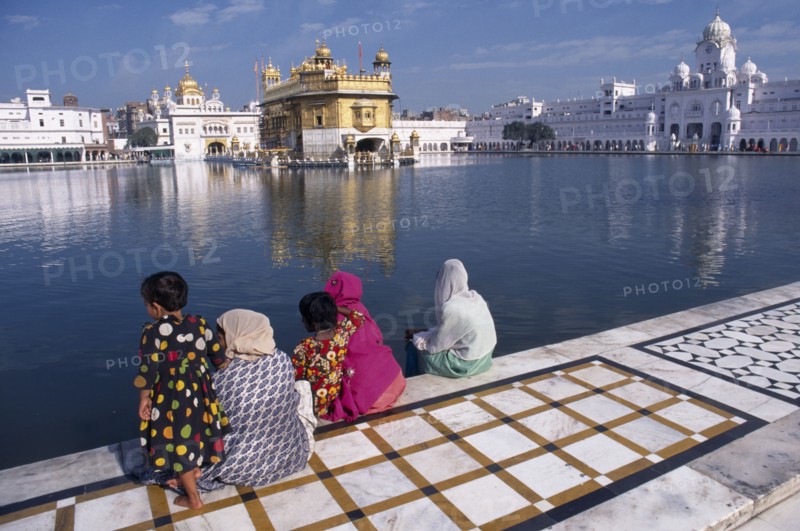 INDIA, Punjab, Amritsar , Golden Temple.  Sikh women and children sitting at the side of the sacred pool looking towards the temple.