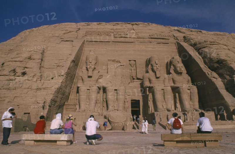 EGYPT, Abu Simbel, Tourists sitting in front of giant seated statues of Ramesses II at temple entrance