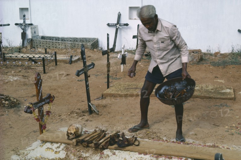 INDIA, Goa, Colva, Man cleaning bones at family grave. The bones are removed and washed to make space for the next family member