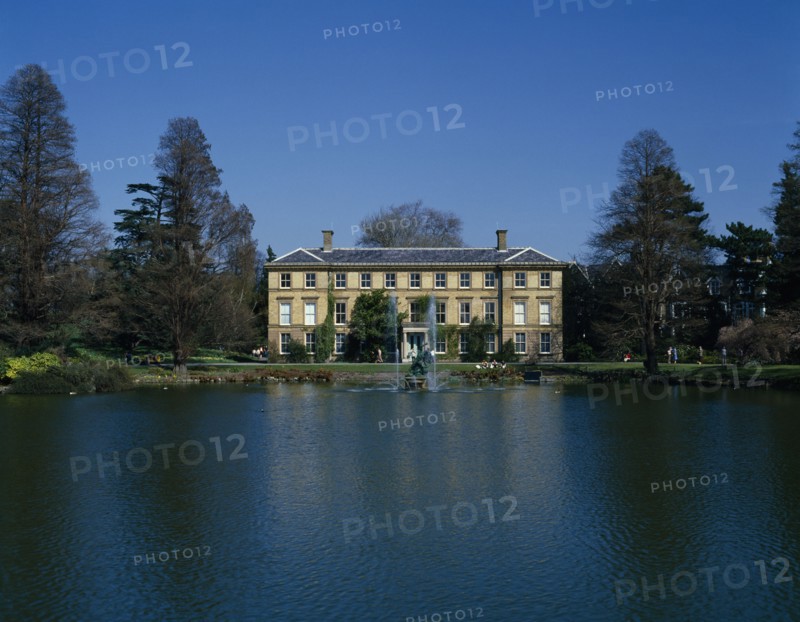 ENGLAND, London, Kew Gardens, View over lake towards large house and fountains with visitors sitting on the banks.