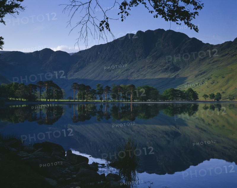 ENGLAND, Cumbria, Lake District, Buttermere.  Rugged hills and trees with mirror reflection in lake.