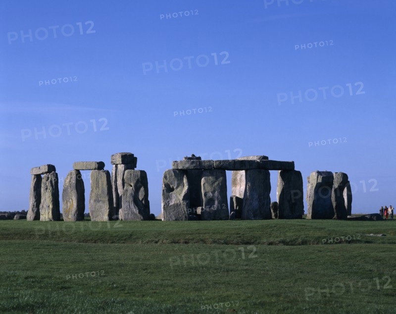 ENGLAND, Wiltshire, Stonehenge, View across the grass on Salisbury Plain toward standing stones with visitors at base