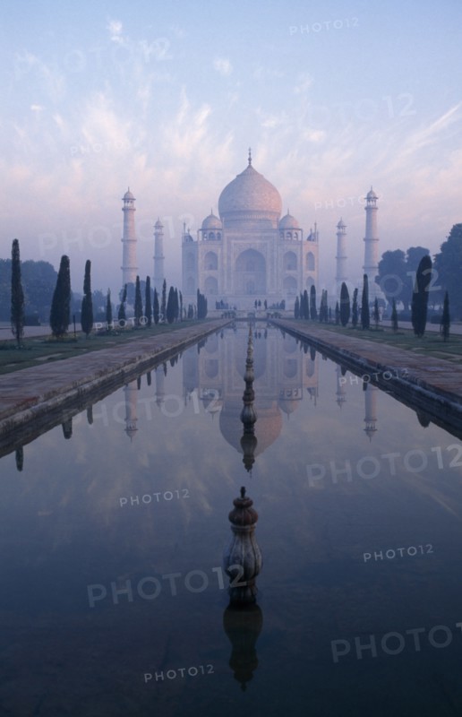 INDIA, Uttar Pradesh, Agra , Taj Mahal reflected in watercourse through formal gardens in pale pink dawn mist.