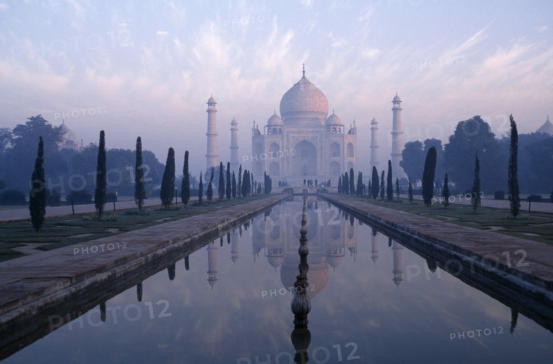 INDIA, Uttar Pradesh, Agra, The Taj Mahal exterior reflected in watercourse through formal gardens in pale pink dawn mist.