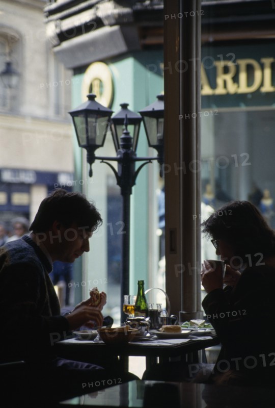 FRANCE, Normandy , Rouen, A back lit couple sat eating and drinking in a Cafe interior.
