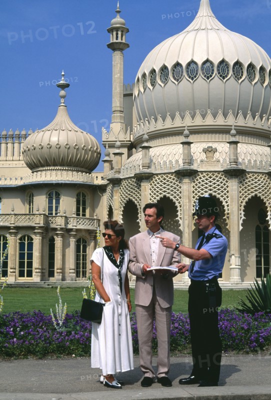 ENGLAND, East Sussex, Brighton, Policeman giving tourist couple directions outside the Royal Pavilion.