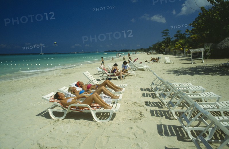 WEST INDIES,  Jamaica, Negril, Female tourists beach sunbathing on sun loungers facing away from the water