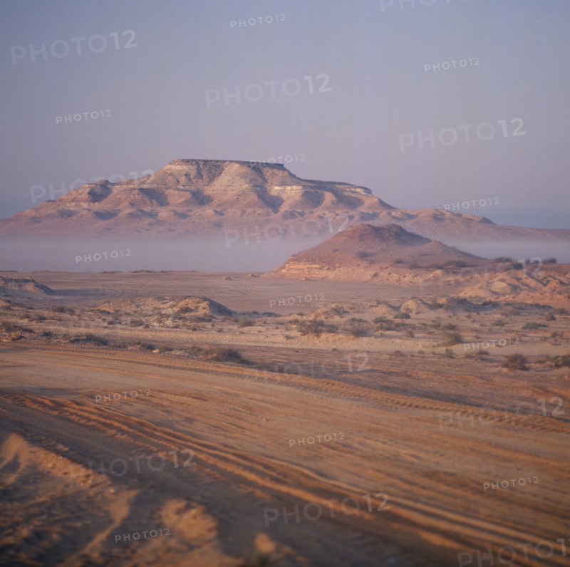 UAE, Abu Dhabi, "Nr Ruwais, Desert and hills with vehicle tracks on flat area in foreground seen on a Misty morning "