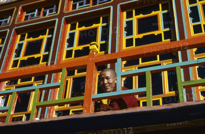 TIBET, Gyantse, Palkhor Choide , Monk looking over brightly painted colourful Monastery  balcony
