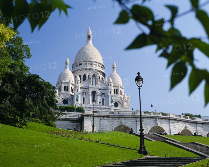 FRANCE, Ile de France, Paris, Sacre Coeur.  Exterior against blue sky partly framed by tree branches.