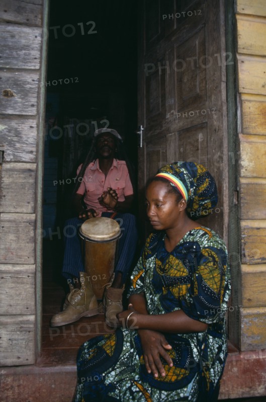 JAMAICA, Music, Percussion, Rastafarian couple with man playing bongo drums inside home while woman sits in open doorway.