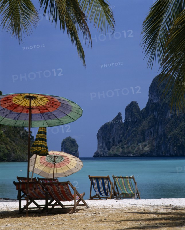 THAILAND, Krabi, Phi Phi Island, Beach in enclosed bay with deckchairs and umbrellas beneath coconut palm trees
