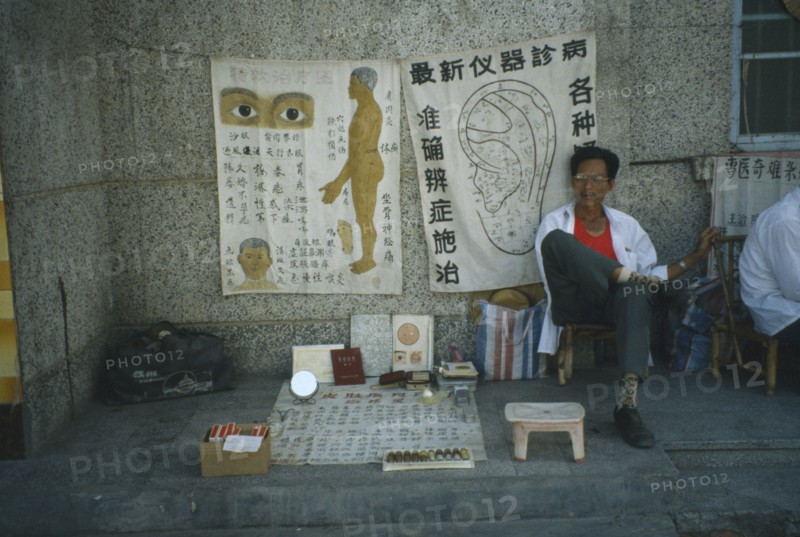 CHINA, Hainan Island, Sanya, Roadside medicine seller seated in front of medical drawings of the human body