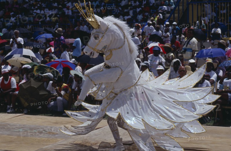 WEST INDIES, Barbados, Crop Over festival celebrating the sugar cane harvest with reveller dressed in horse costume parading in front of crops.