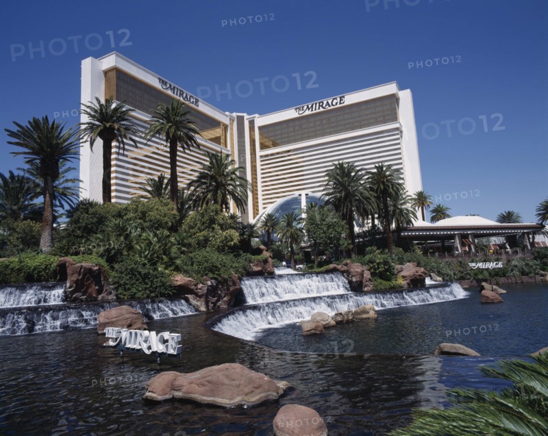 USA, Nevada, Las Vegas, Mirage Hotel and Casino. View across waterfall and palm tree lined rock pool to hotel entrance.