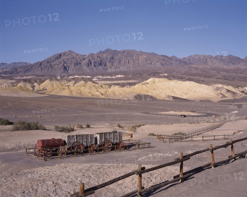 USA, California, Death Valley, Historic Harmony Borax Works. Wooden containers and steel cylinder on trailers in fenced area in desert landscape with hills in the background