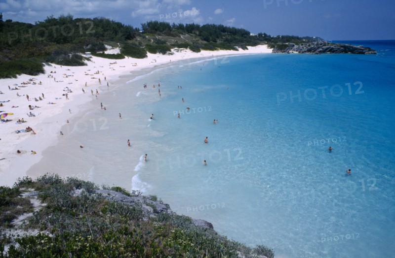 BERMUDA, Southampton, Horseshoe Bay, View over bay lined by sandy beach and vegetation with people sunbathing and in the water.
