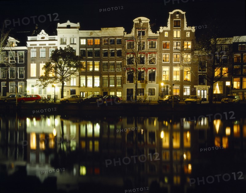 HOLLAND, North, Amsterdam, Canalside houses and lights reflected in water at night.